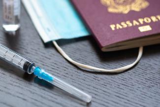 Syringe with needle, vial, surgical face mask and passport or visa on a white table ready to be used. Covid or Coronavirus vaccine background By Michele Ursi